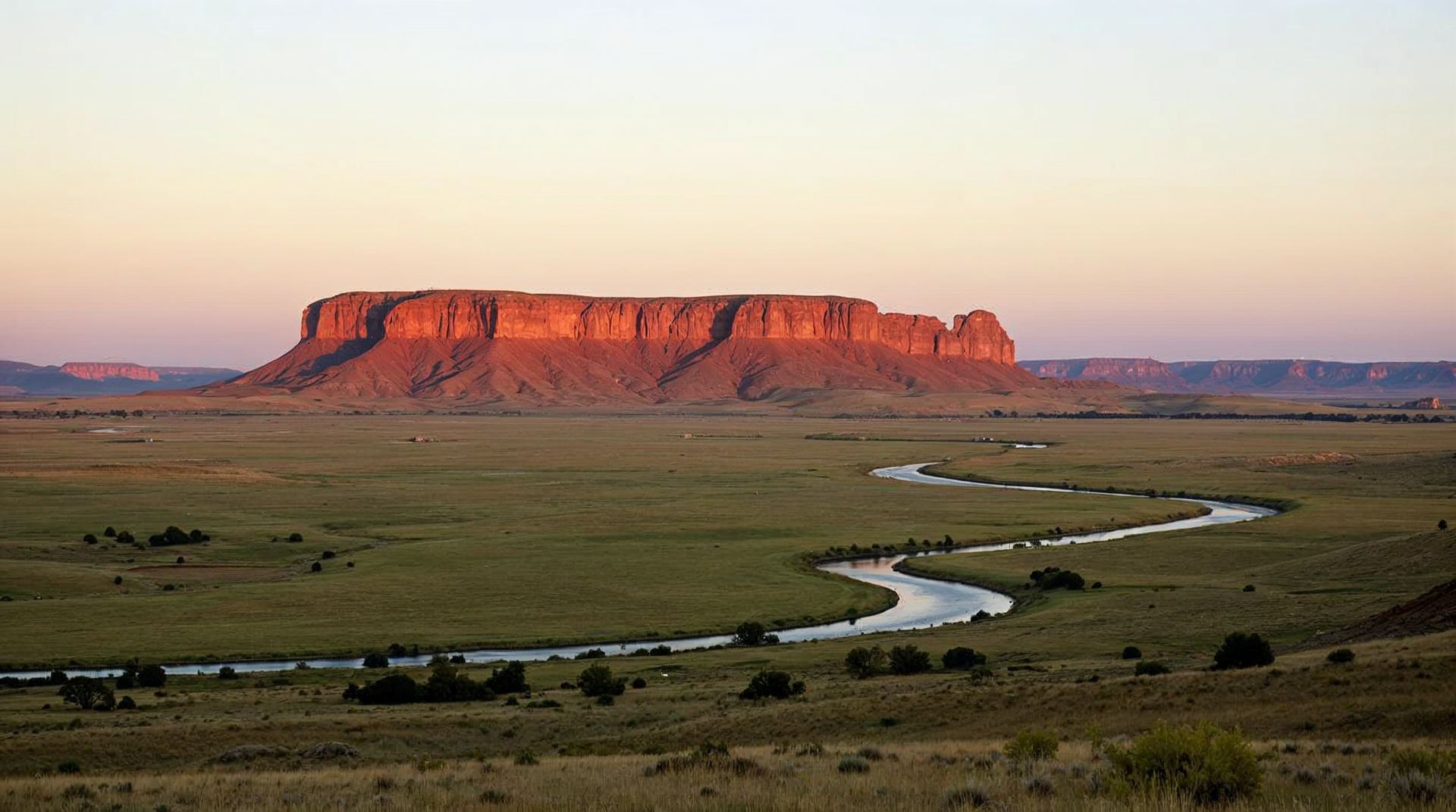Scotts Bluff National Monument glowing orange at sunrise above green prairie in Nebraska
